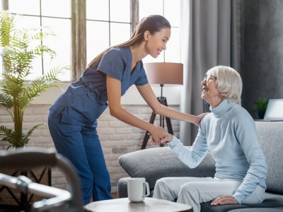 Happy female professional caregiver taking care of elderly woman at home